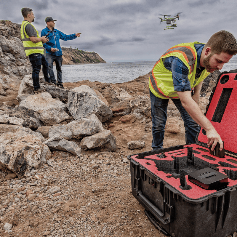 Technicians deploying a drone for coastal inspection and environmental monitoring, with rugged terrain and shoreline in the background.