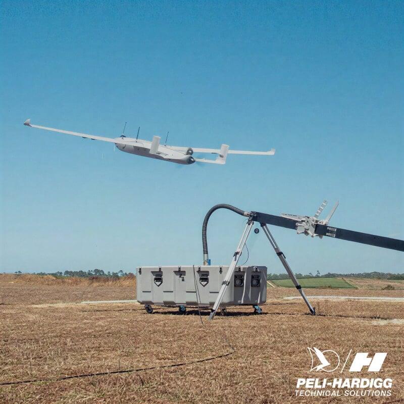 Tekever fixed-wing drone being launched from a ground-based catapult system in an open field under clear blue sky.