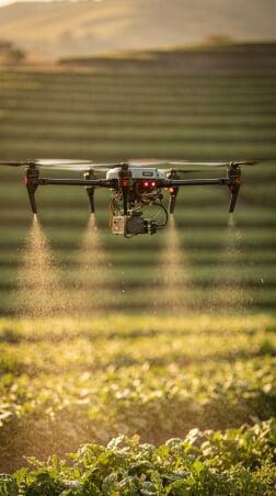 Agricultural drone spraying crops with precision farming technology over a green field during sunset, used for smart farming and crop management.
